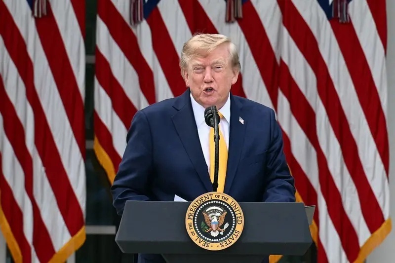 Donald Trump de pie ante un podio. Viste traje azul, camisa blanca y corbata amarilla. En el fondo hay una serie de banderas de fanjas blancas y rojas.Fuente de la imagen,Getty Images Pie de foto,Trump festejó el acuerdo como 